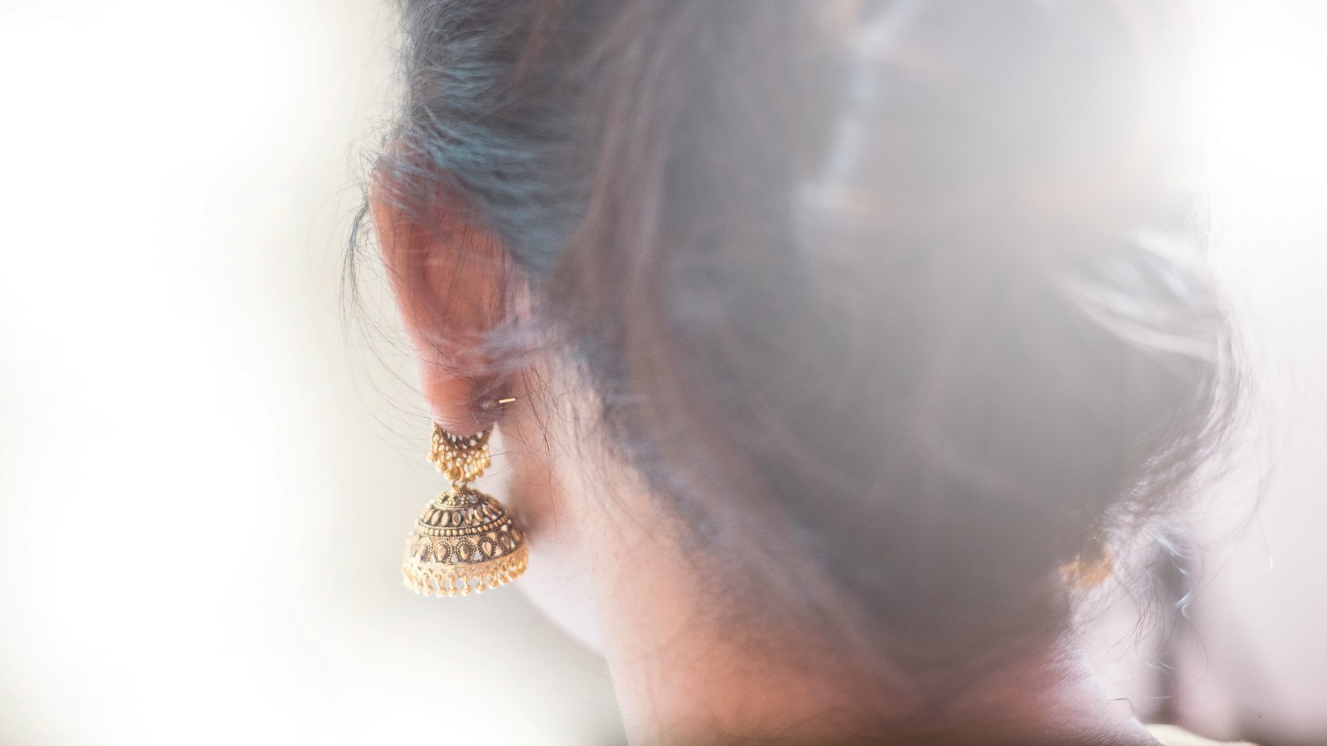 Woman's ear, wearing a gold jhumka.